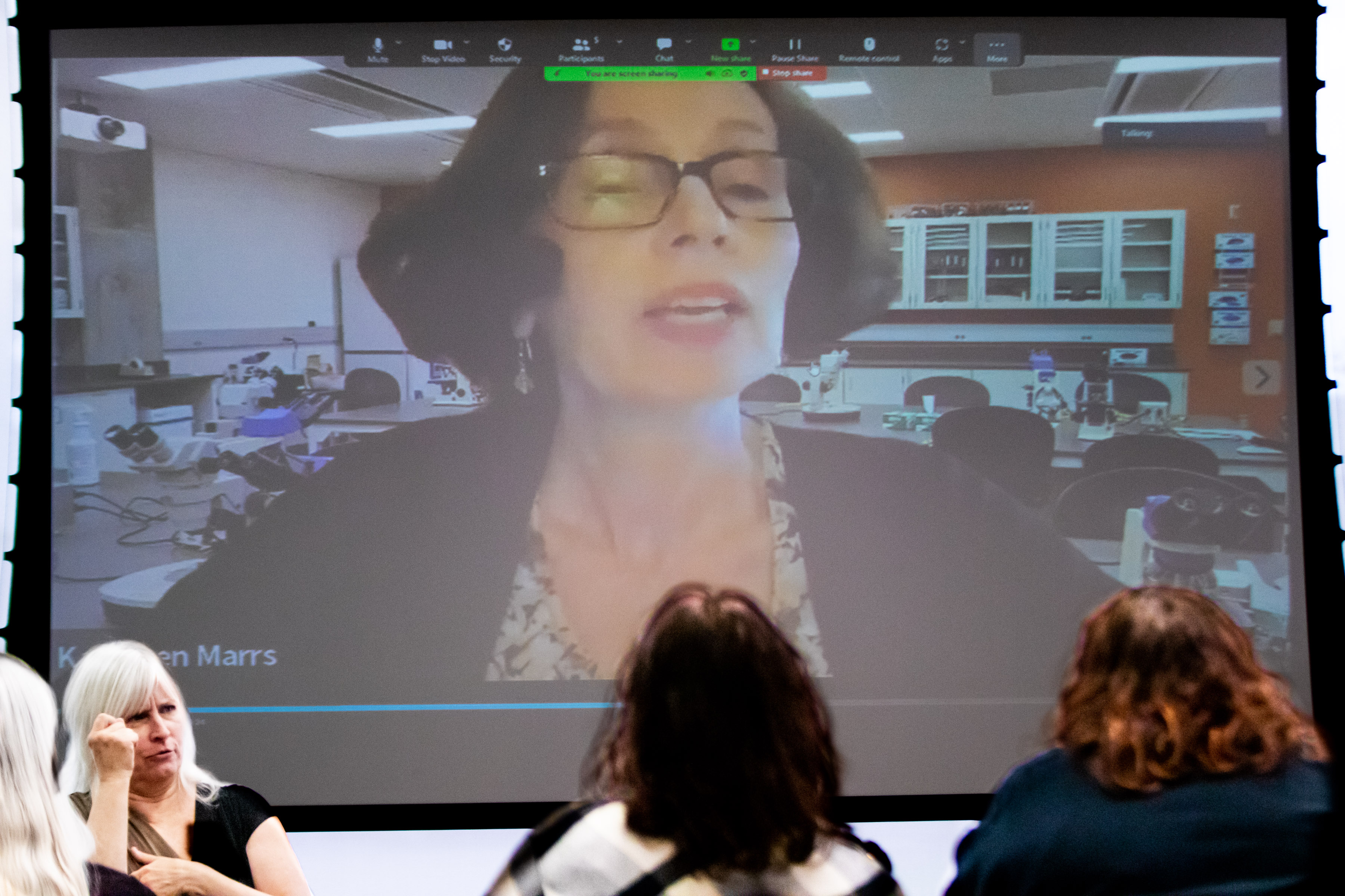 View from behind attendees of large screen with recording of faculty member and view of ASL interpreter