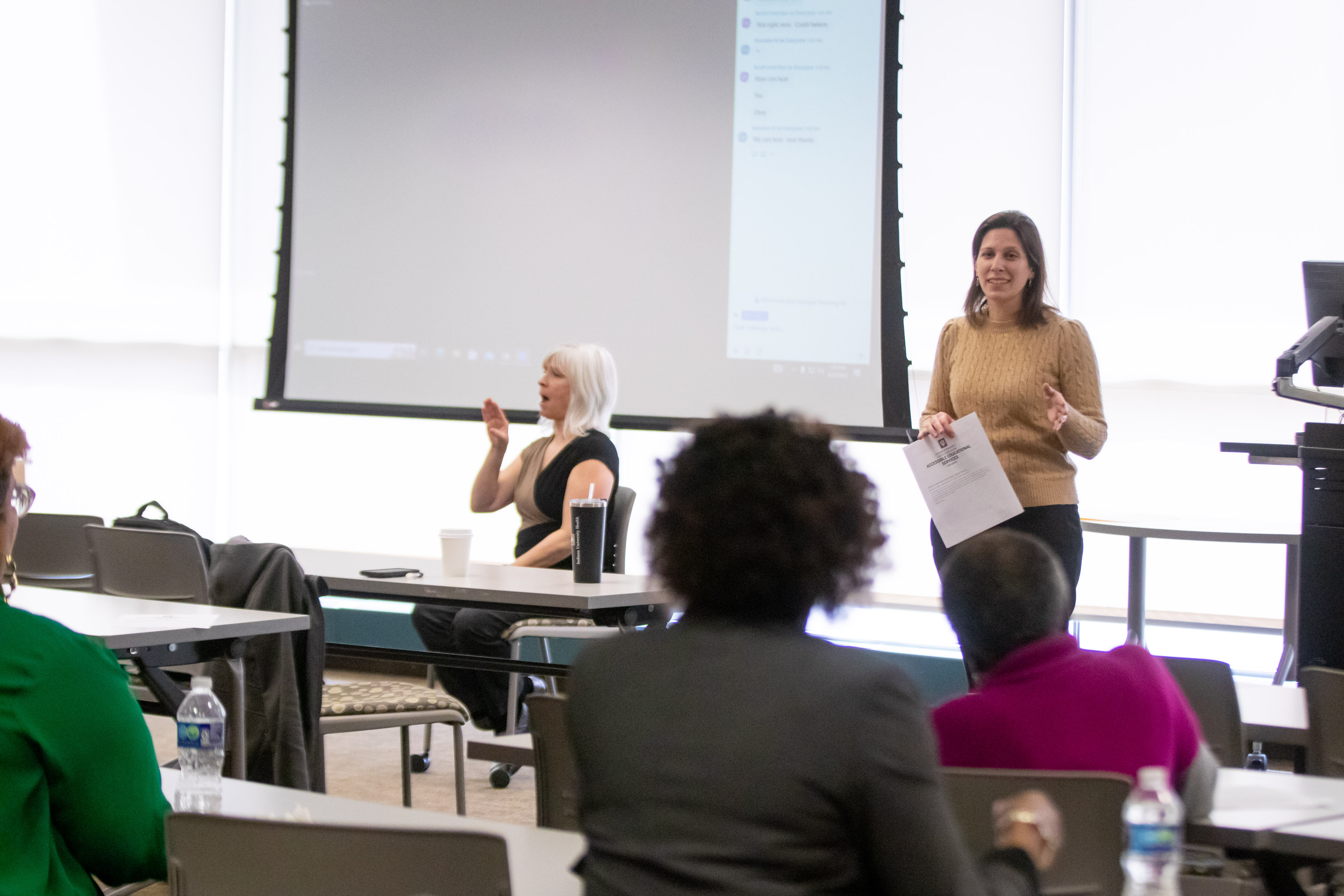 View of the speaker standing up giving speech with view of ASL interpreter sitting down beside her