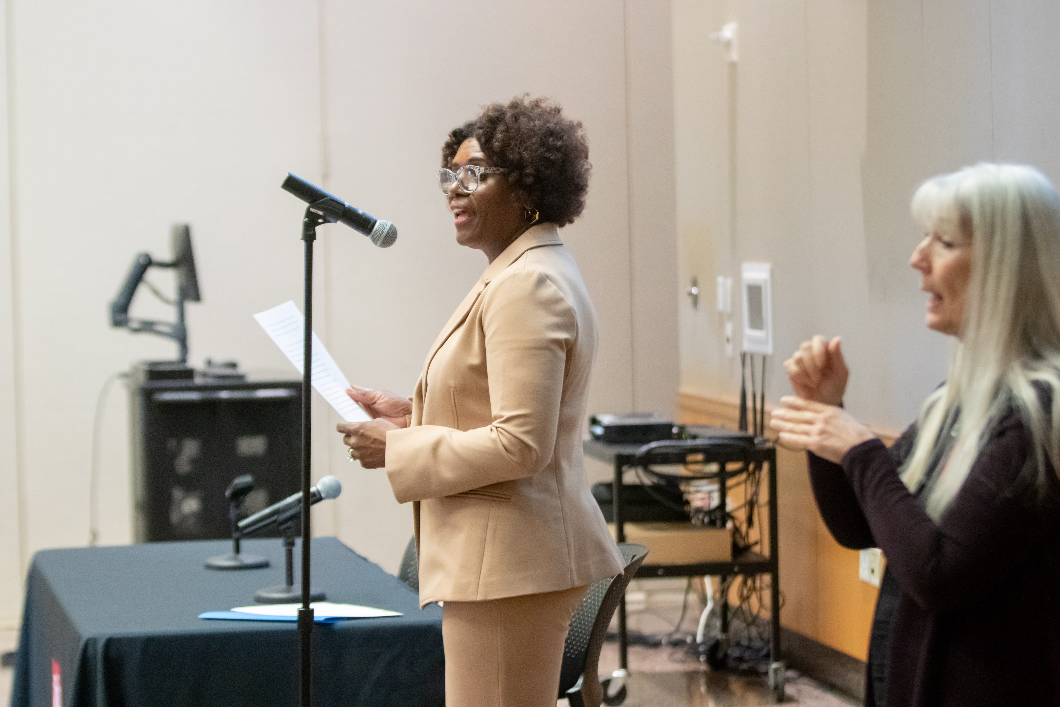 Side view of Director of AES, Dr. Mercedes Cannon, giving her introduction smiling with glasses on and ASL interpreter mid sentence