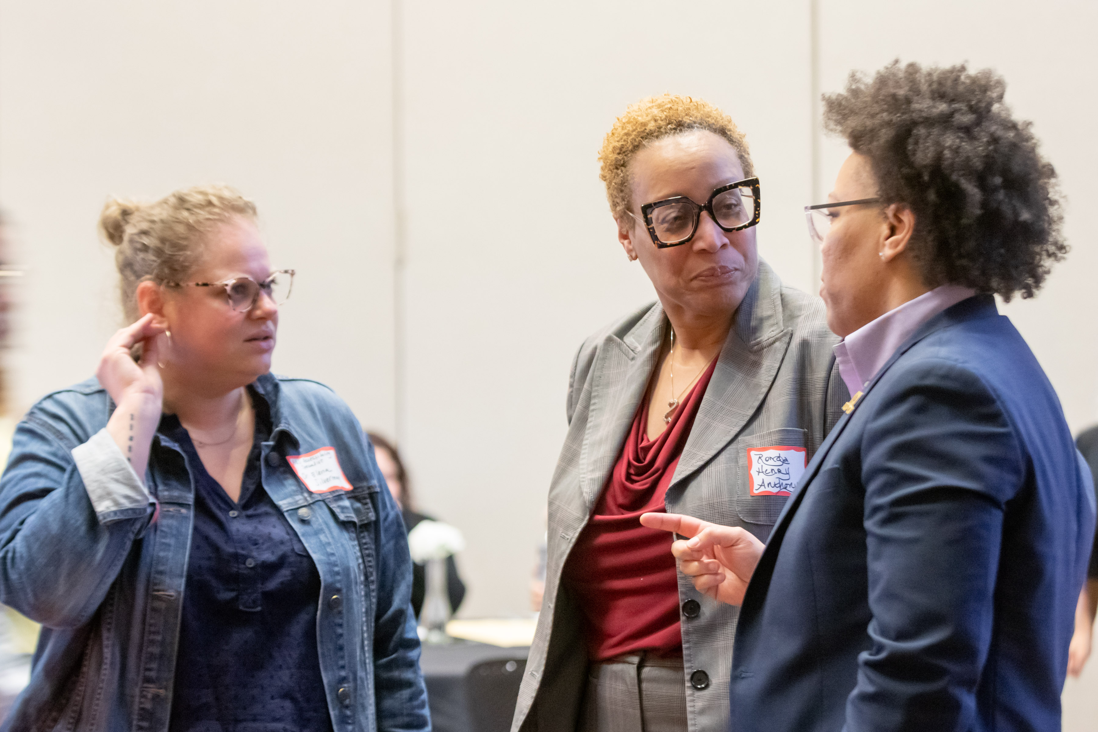 Three well dressed attendees stand in half circle engrossed in conversation 